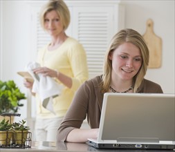 Mother watching teenaged daughter typing on computer.