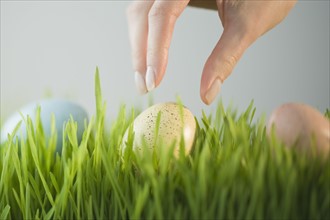 Woman reaching for decorated egg in grass.