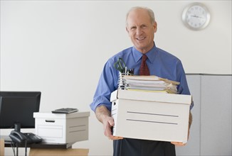 Senior businessman carrying box and office supplies.