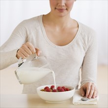Woman pouring milk on cereal.