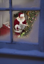 Santa Claus leaving gifts under Christmas tree.