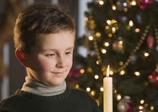 Boy looking at candle in front of Christmas tree.