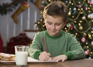 Boy writing letter in front of Christmas tree.