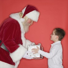 Santa Claus handing gift to boy.