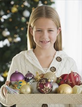 Girl holding box of Christmas ornaments.