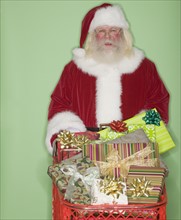 Santa Claus pushing shopping cart of gifts.