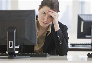 Frustrated businesswoman leaning on desk.