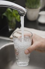 Man filling glass of water at sink.