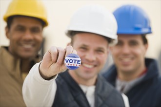 Multi-ethnic construction workers with Vote button.