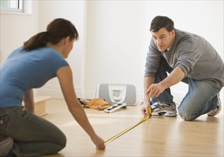 Couple measuring floor with tape measure.