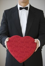 Man in tuxedo holding heart shaped box.