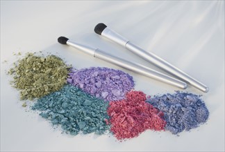 Assorted crushed cosmetics next to brushes.
