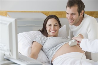 Pregnant Hispanic couple looking at ultrasound monitor.