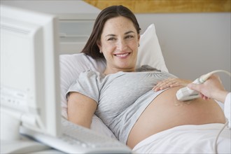 Pregnant Hispanic woman looking at ultrasound monitor.