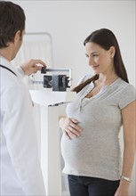 Pregnant Hispanic woman on scale in doctor’s office.