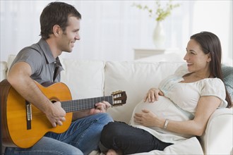 Hispanic man playing guitar for pregnant wife.