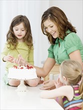 Mother and daughters decorating birthday cake. Date : 2008