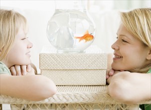Mother and daughter looking at fish in bowl. Date : 2008