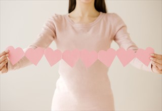 Woman holding string of cut out hearts. Date : 2008