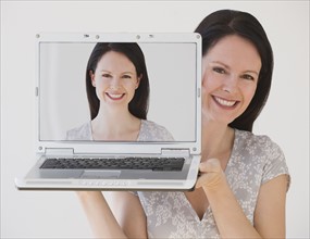 Woman holding laptop next to face.