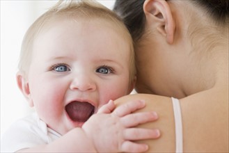 Baby laughing over mother’s shoulder. Date : 2008