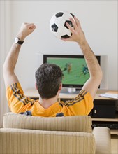 Man with soccer ball cheering at television.