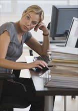 Businesswoman with stack of paperwork on desk.