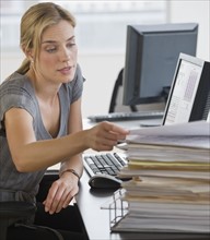 Businesswoman with stack of paperwork on desk.