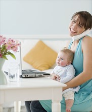 Mother holding baby and working at home. Date : 2008