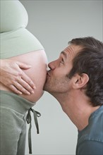 Hispanic man kissing pregnant wife’s belly.