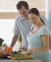 Pregnant Hispanic couple preparing food.