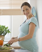 Pregnant Hispanic woman chopping vegetables.