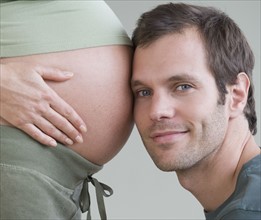 Hispanic man resting head on pregnant wife’s belly.