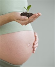 Pregnant woman holding soil and plant.