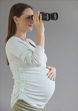 Pregnant Hispanic woman looking through binoculars.