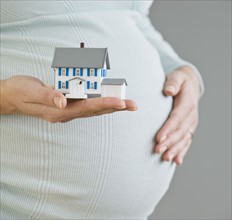 Pregnant woman holding model house.