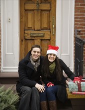 Couple with Christmas tree and gifts in front of door. Date : 2008