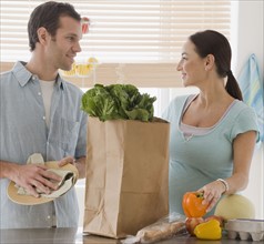 Pregnant Hispanic couple unpacking groceries.