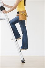 Woman wearing tool belt climbing ladder.