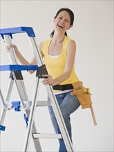 Woman wearing tool belt climbing ladder.