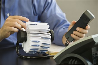 Businessman holding telephone and looking at card file.