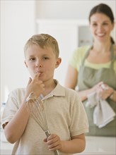 Boy licking finger and holding whisk.