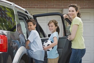 Mother and children getting into car with soccer ball.