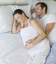 Pregnant Hispanic couple sleeping in bed.