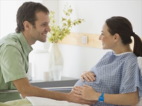 Pregnant Hispanic couple smiling at each other.