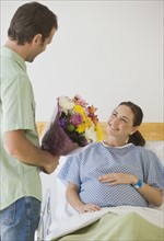 Hispanic man giving flowers to pregnant wife.
