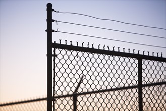 Silhouette of barbed wire and chain-link fence. Date : 2008