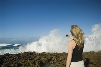 Woman taking photograph of ocean, Oahu, Hawaii, United States. Date : 2008