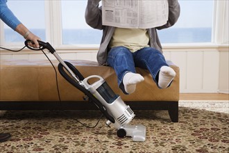Woman vacuuming under man’s feet. Date : 2008