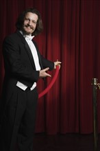 Man in tuxedo holding velvet rope. Date : 2008